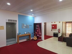 A lobby with a blue wall, a sign reading 'ibis', a guitar, a red carpet, and a fire extinguisher. - ibis Setubal (Setubal)