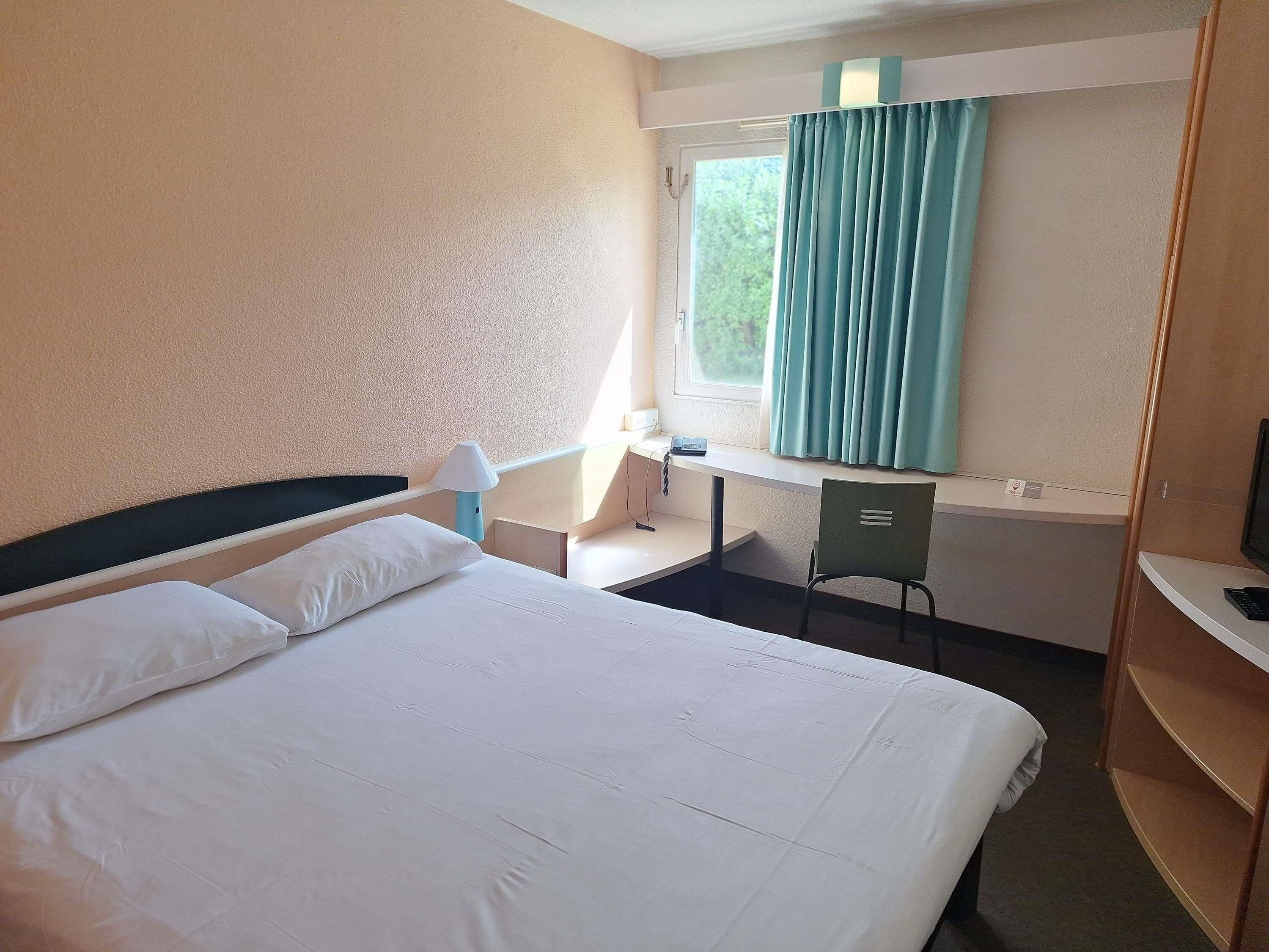 A hotel room with a bed, desk, chair, and a window with curtains.