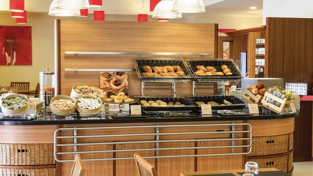 A buffet setup with various food items, a coffee machine, and a seating area with chairs and tables. - ibis Setubal (Setubal)