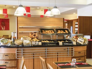 A buffet setup with various food items, a coffee machine, and a seating area with chairs and tables. - ibis Setubal (Setubal)