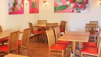 A dining area with wooden tables and chairs, red cushions, and wall-mounted lamps.