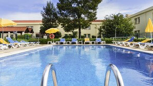 A swimming pool with sun loungers and umbrellas, surrounded by trees and a building. - ibis Setubal (Setubal)