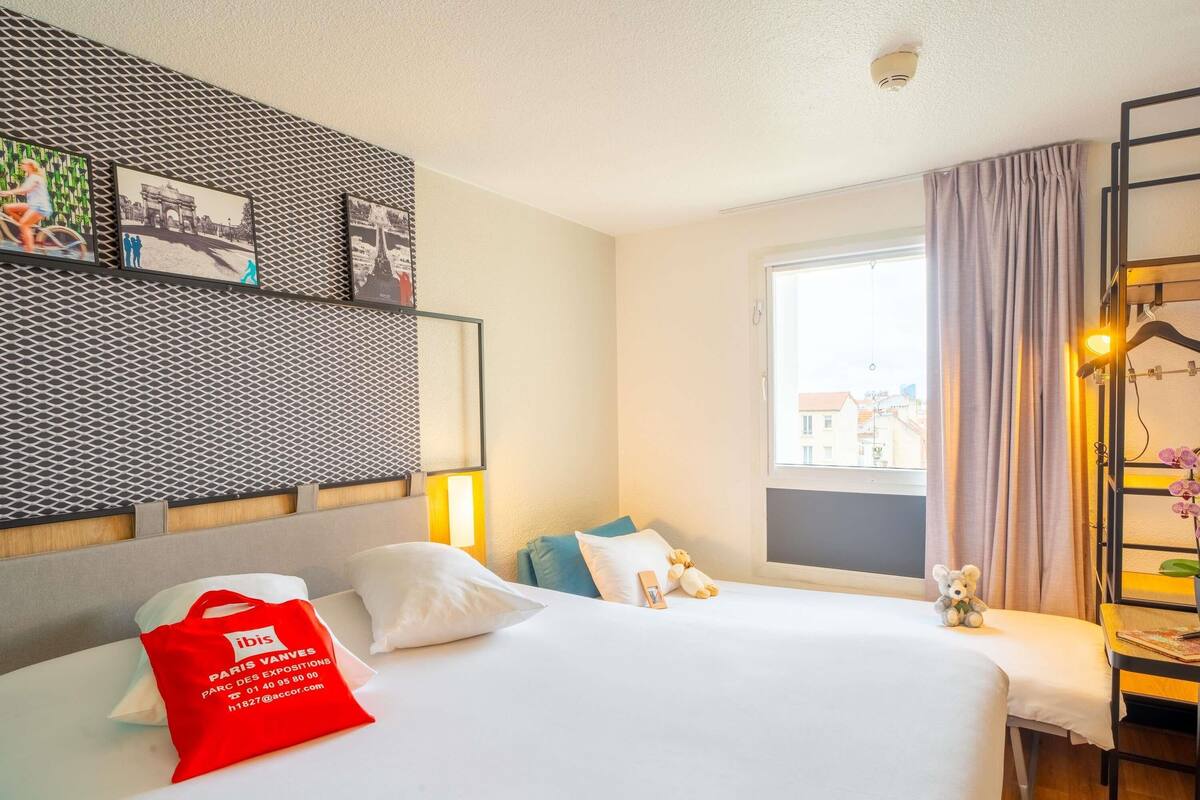 Une chambre d’hôtel avec un lit, un bureau, une fenêtre avec des rideaux et des œuvres d’art murales.
