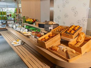 Un buffet proposant une variété de plats, notamment des fruits, des pâtisseries et du pain.