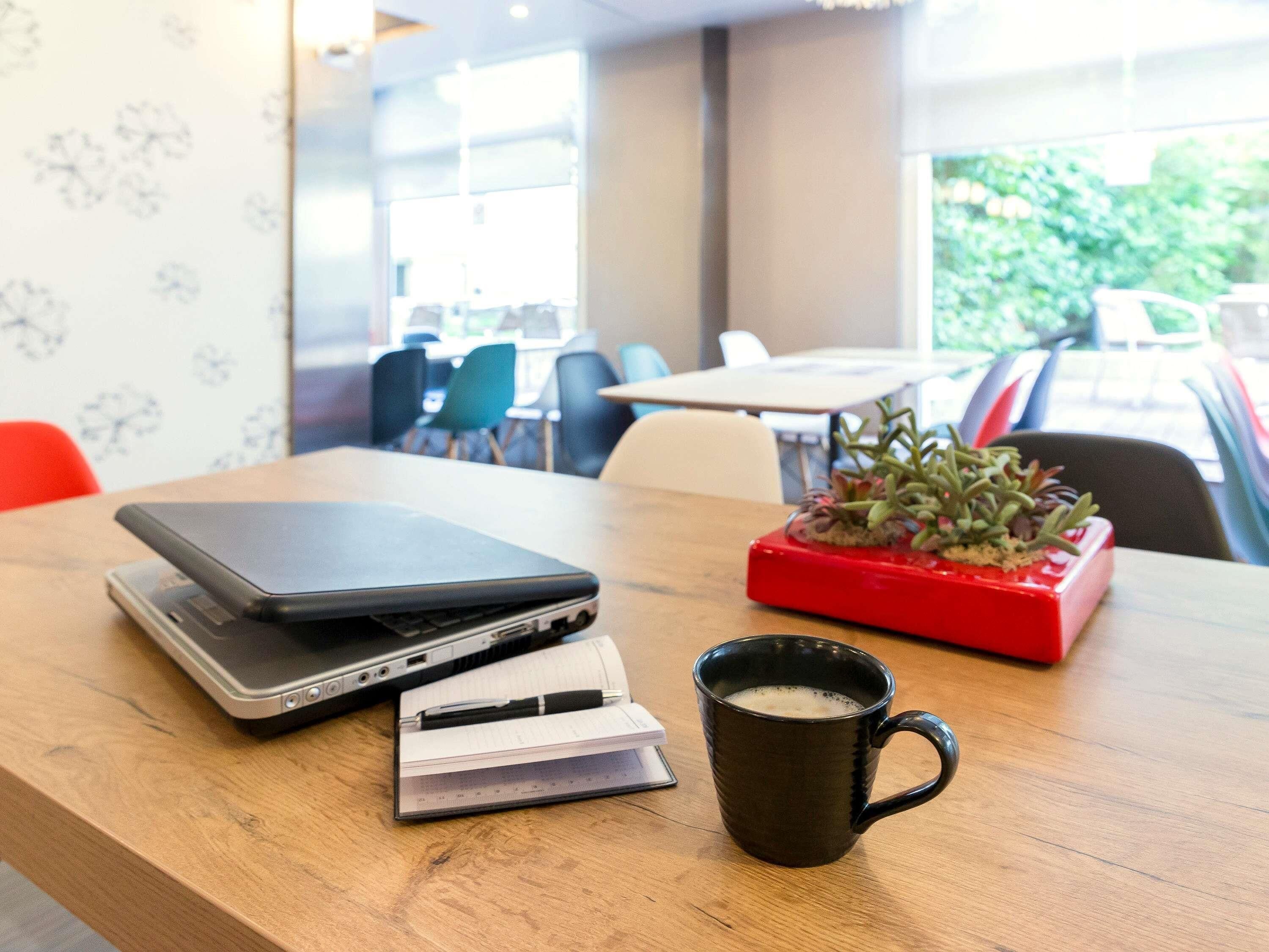 A wooden table with a laptop, a notebook, a pen, a mug, and a red planter with plants.