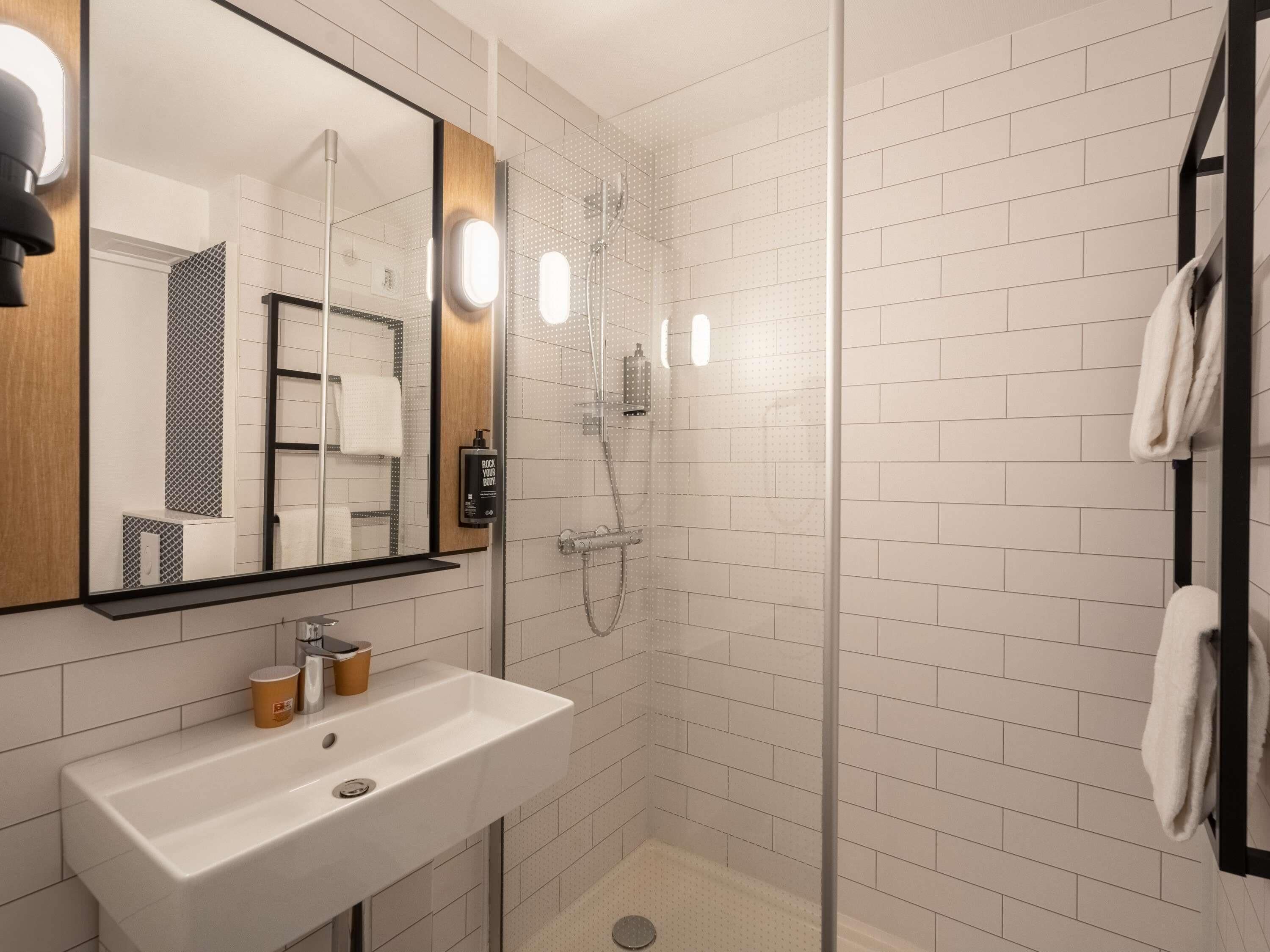 A modern bathroom with a white sink, a mirror, a glass shower enclosure, and a towel rack.