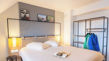 A hotel room with a bed, a side table, a wall-mounted shelf with pictures, and a built-in wardrobe.