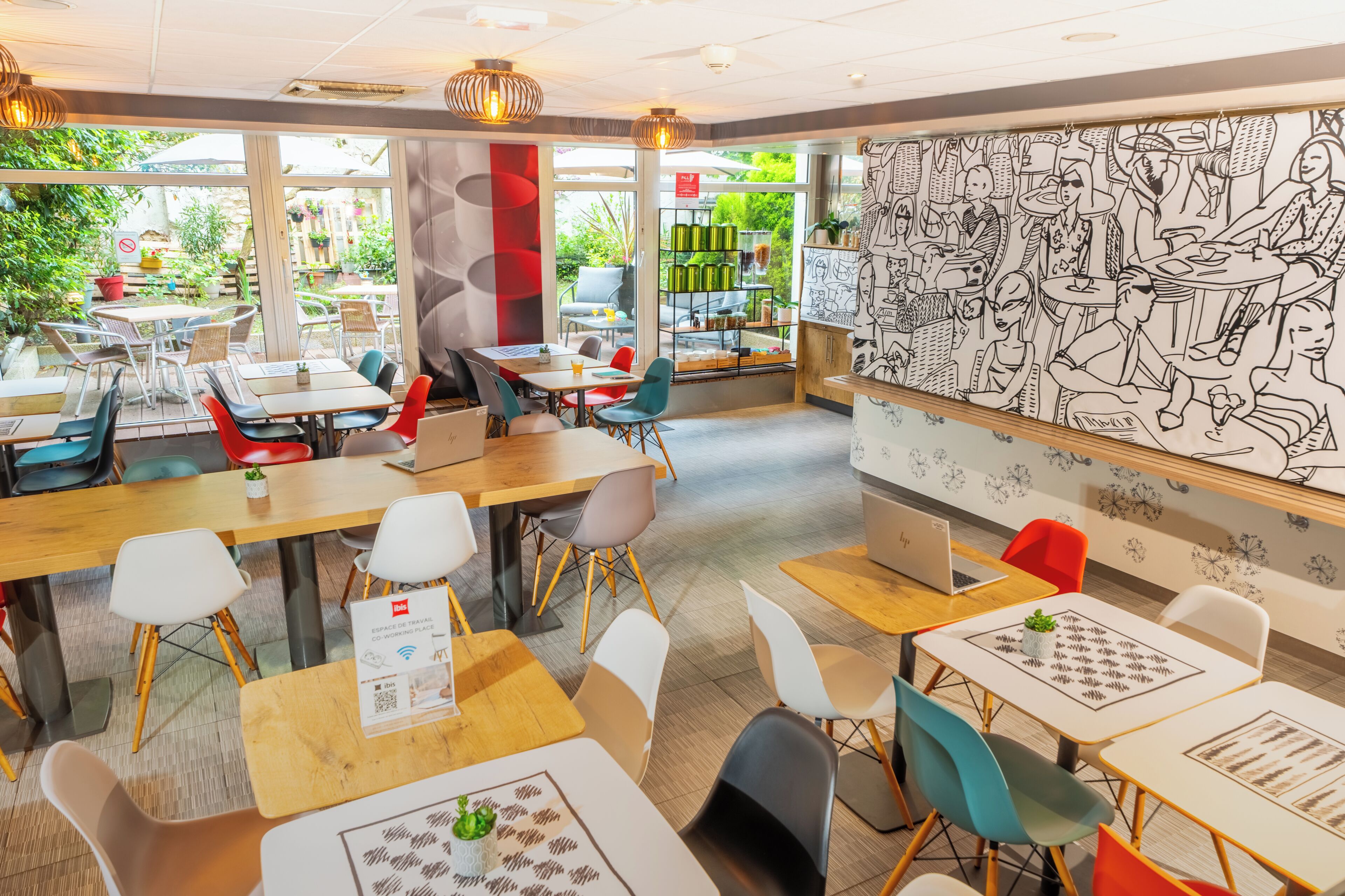 Una cafetería moderna con mesas y sillas, un ventanal grande y una pared con un mural en blanco y negro.