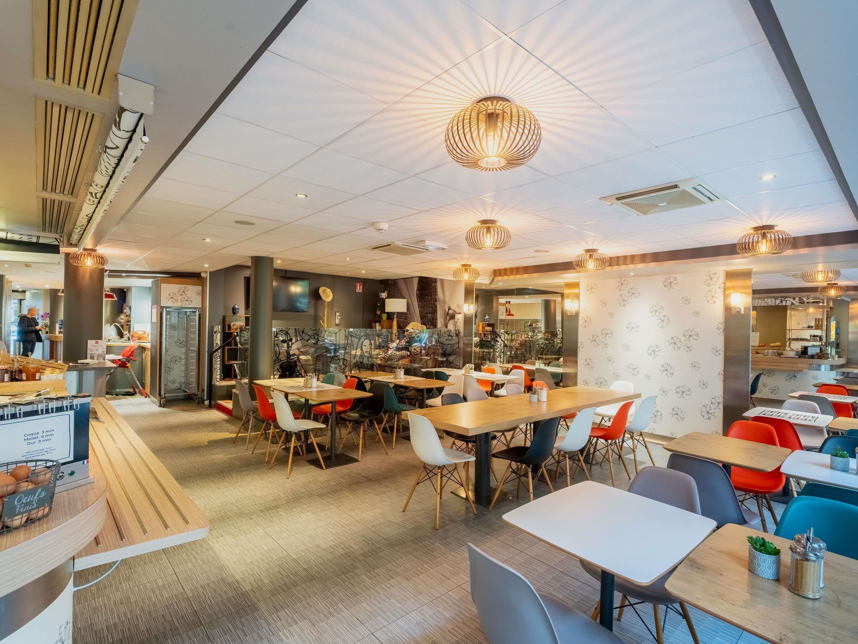 A modern restaurant with multiple dining areas, wooden tables, and colorful chairs.