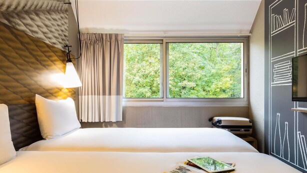 Una habitación de hotel con una cama, un ventanal con vistas a la vegetación, una lámpara y una pared con diseño de pizarra.