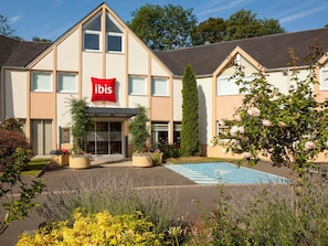 Un hôtel reconnaissable à son grand panneau rouge avec le logo ibis, doté d’une entrée aménagée et d’une piscine.