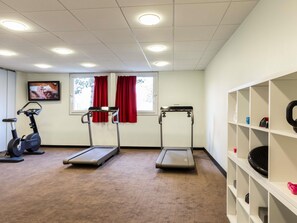 A room with exercise equipment, a television, and a window with curtains. - Ibis Jouy en Josas Velizy (Jouy-en-Josas)