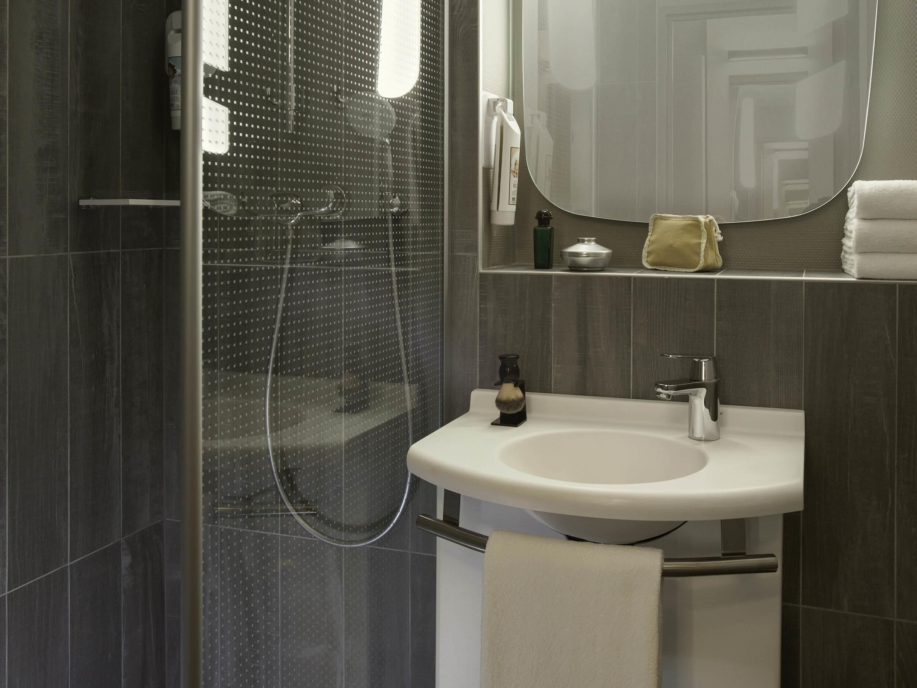 A modern bathroom with a glass-enclosed shower, a white sink, and a mirror above it.