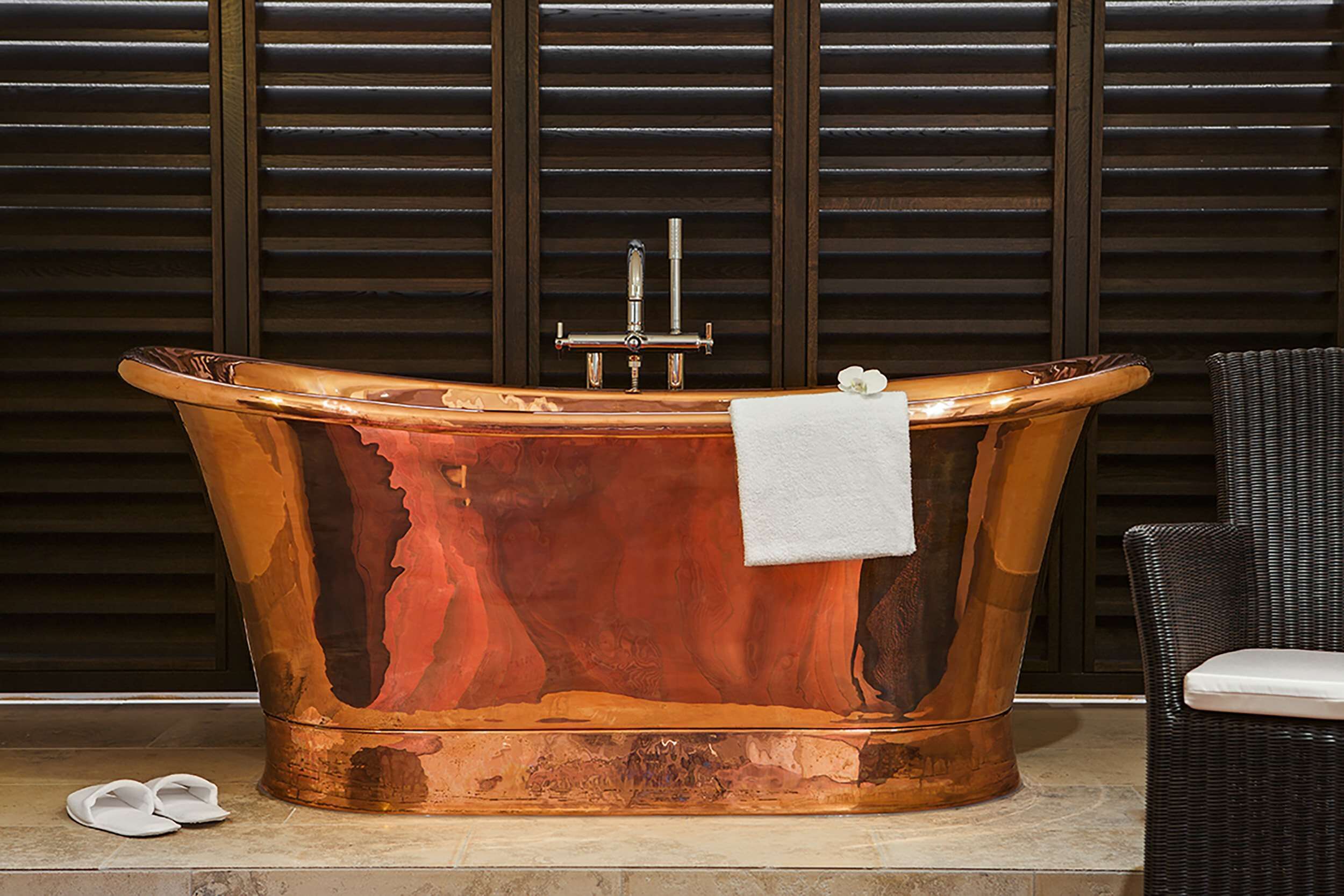 A freestanding copper bathtub with a faucet and a white towel.