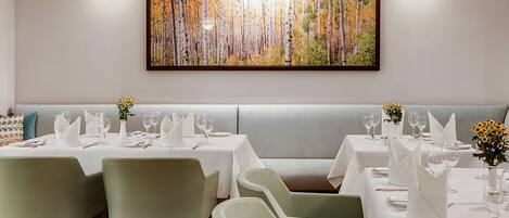 A restaurant with a long table set for a meal, a bench seating area, and a large painting on the wall.