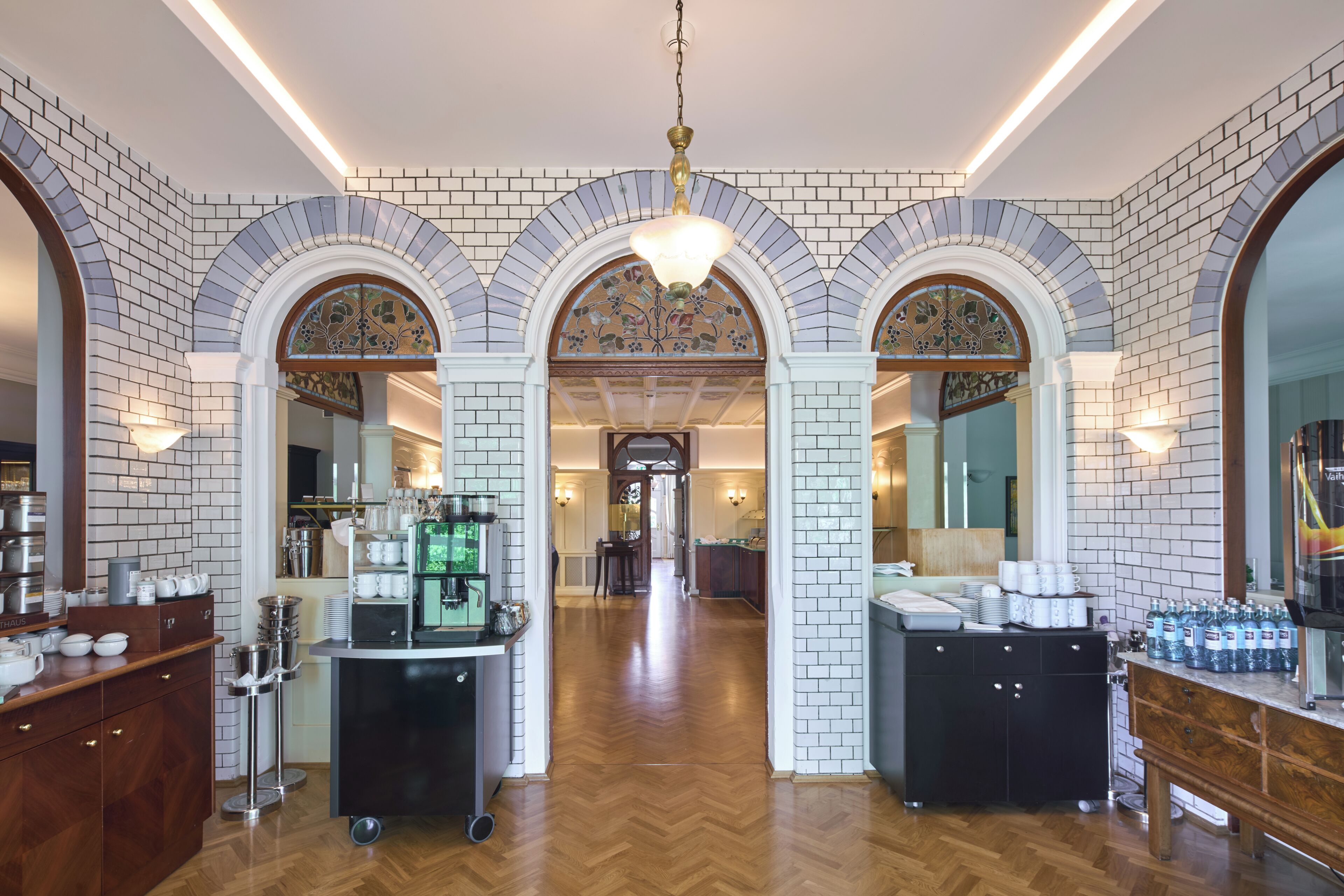 Un vestíbulo de hotel con un pasillo central flanqueado por paredes de ladrillo y arcos, que conduce a varias habitaciones.