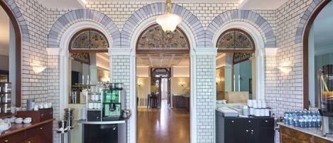 Un vestíbulo de hotel con un pasillo central flanqueado por paredes de ladrillo y arcos, que conduce a varias habitaciones.