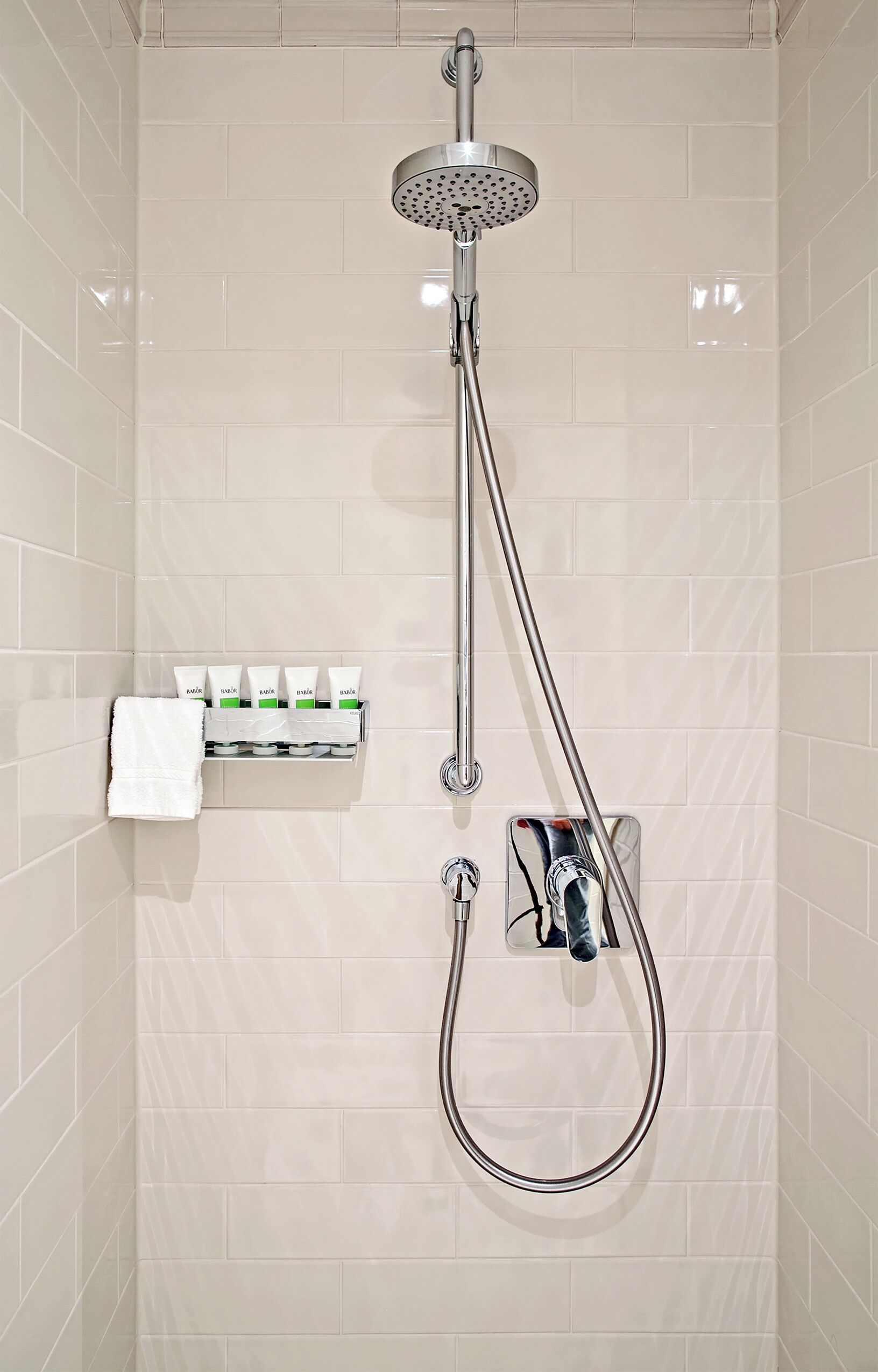 A shower with a handheld showerhead, a wall-mounted faucet, and a soap dispenser.