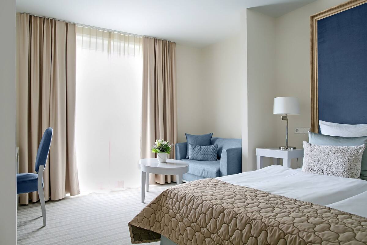 A hotel room with a bed, a chair, a small table with a plant, a sofa, and a lamp.