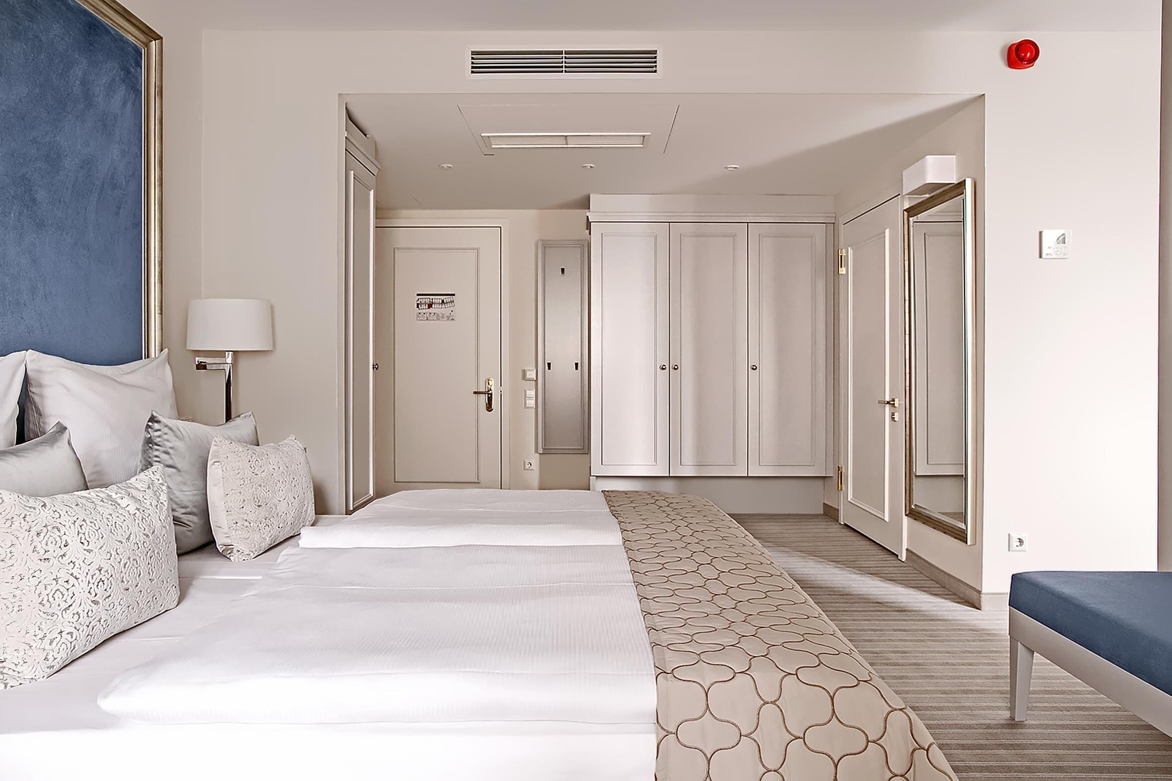 A hotel room with a large bed, a bedside table, a lamp, a wardrobe, and a mirror.