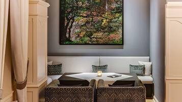 A room with a white sofa, patterned armchairs, and a painting of a forest on the wall.