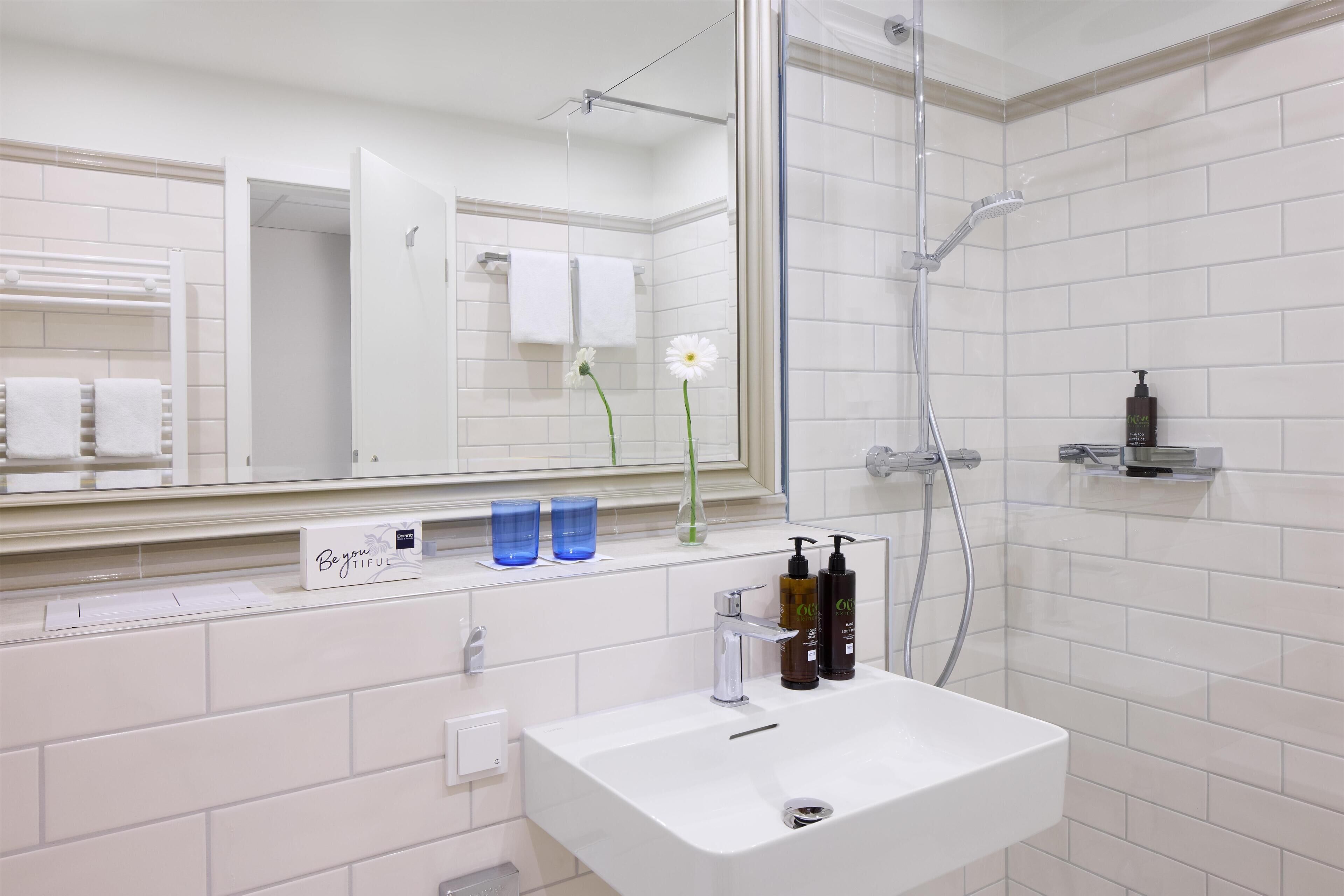 Un baño con lavamanos blanco, espejo, ducha y toallero.
