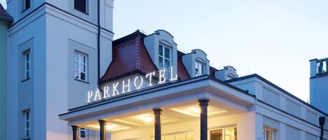 Un hotel con un ingresso imponente, una torre e un cartello con scritto 'PARKHOTEL'.