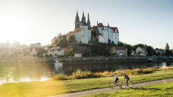 A riverside view with a historic castle and a paved path where two cyclists are riding.