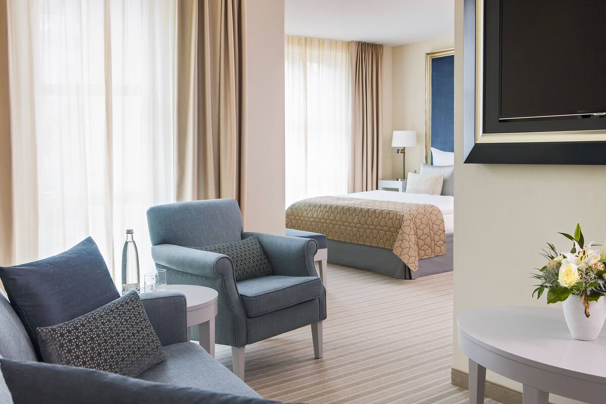 A hotel room with a bed, a sofa, a chair, a small table, and a TV.