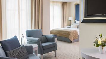 A hotel room with a bed, a sofa, a chair, a small table, and a TV.