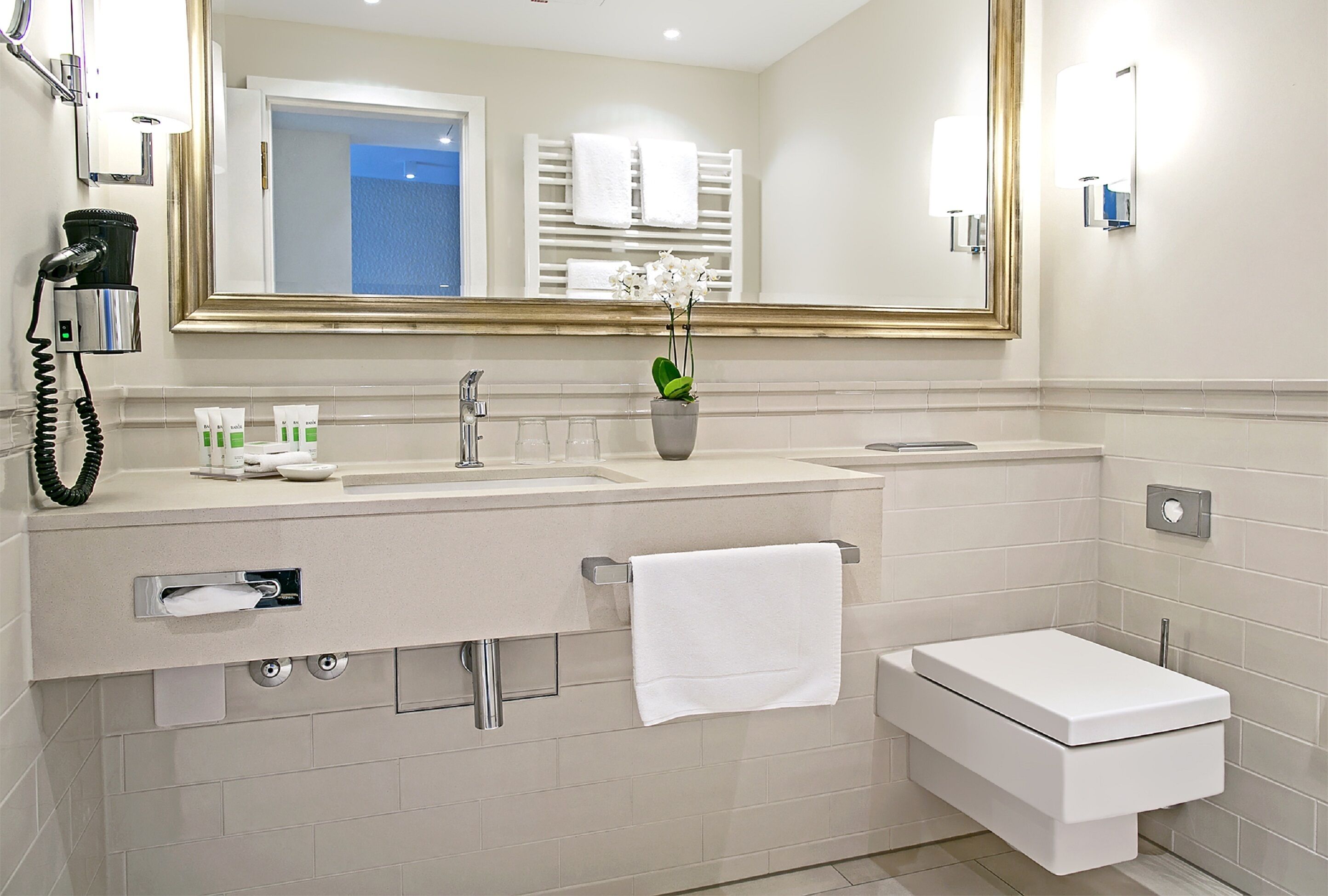 A modern bathroom with a large mirror, a sink with toiletries, a toilet, and a towel rack.