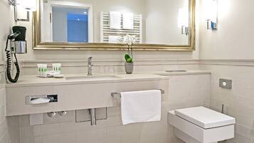 A modern bathroom with a large mirror, a sink with toiletries, a toilet, and a towel rack.