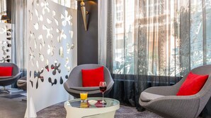 Une pièce moderne avec deux fauteuils gris, une table basse en verre surmontée d’un coussin rouge et un panneau décoratif mural.