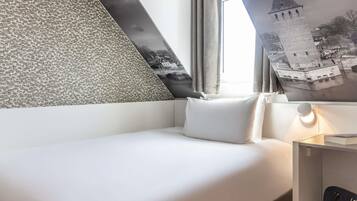 A hotel room with a bed, a nightstand with a lamp, a wall with a patterned design, and a window with curtains.