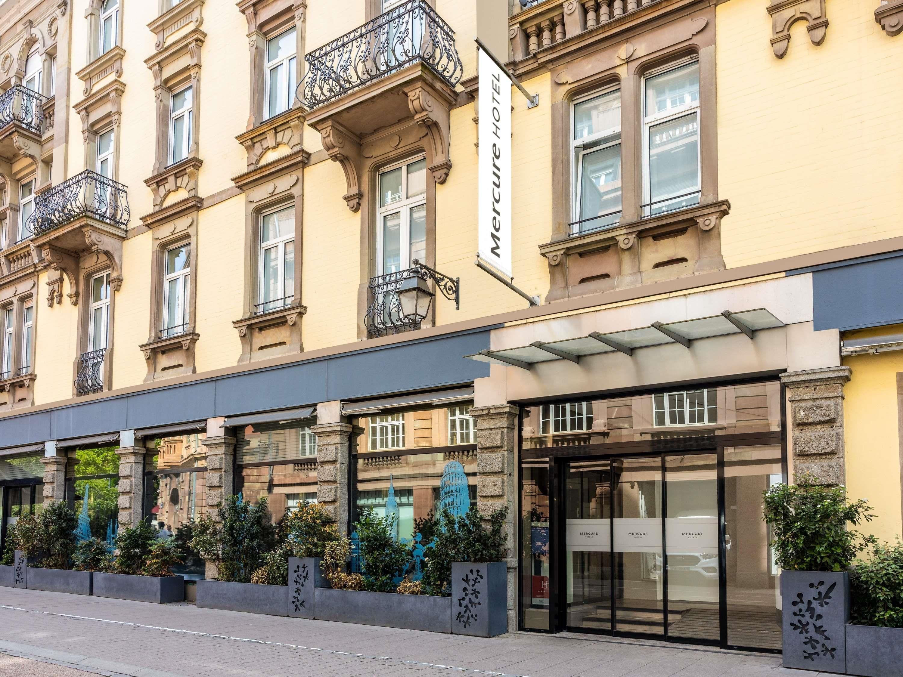 Ein Hotel Eingang mit Glastür, einem Schild darüber und einem Balkon mit schmiedeeisernen Geländern.