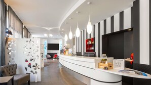 Un espace d’accueil moderne, avec un comptoir d’accueil incurvé, un coin salon comprenant un canapé et des fauteuils, un téléviseur fixé au mur et un présentoir à boissons rouge.
