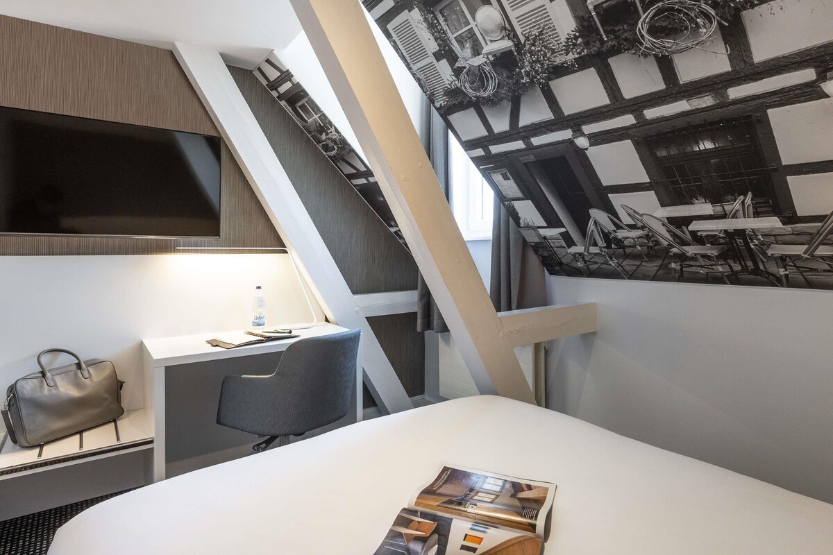 Une chambre d’hôtel avec un lit, un bureau, une chaise, un sac à main et un magazine posé sur le lit.