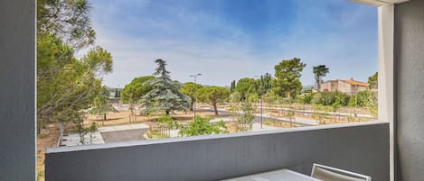 A balcony with a table and chairs, overlooking a landscaped area with trees and buildings.