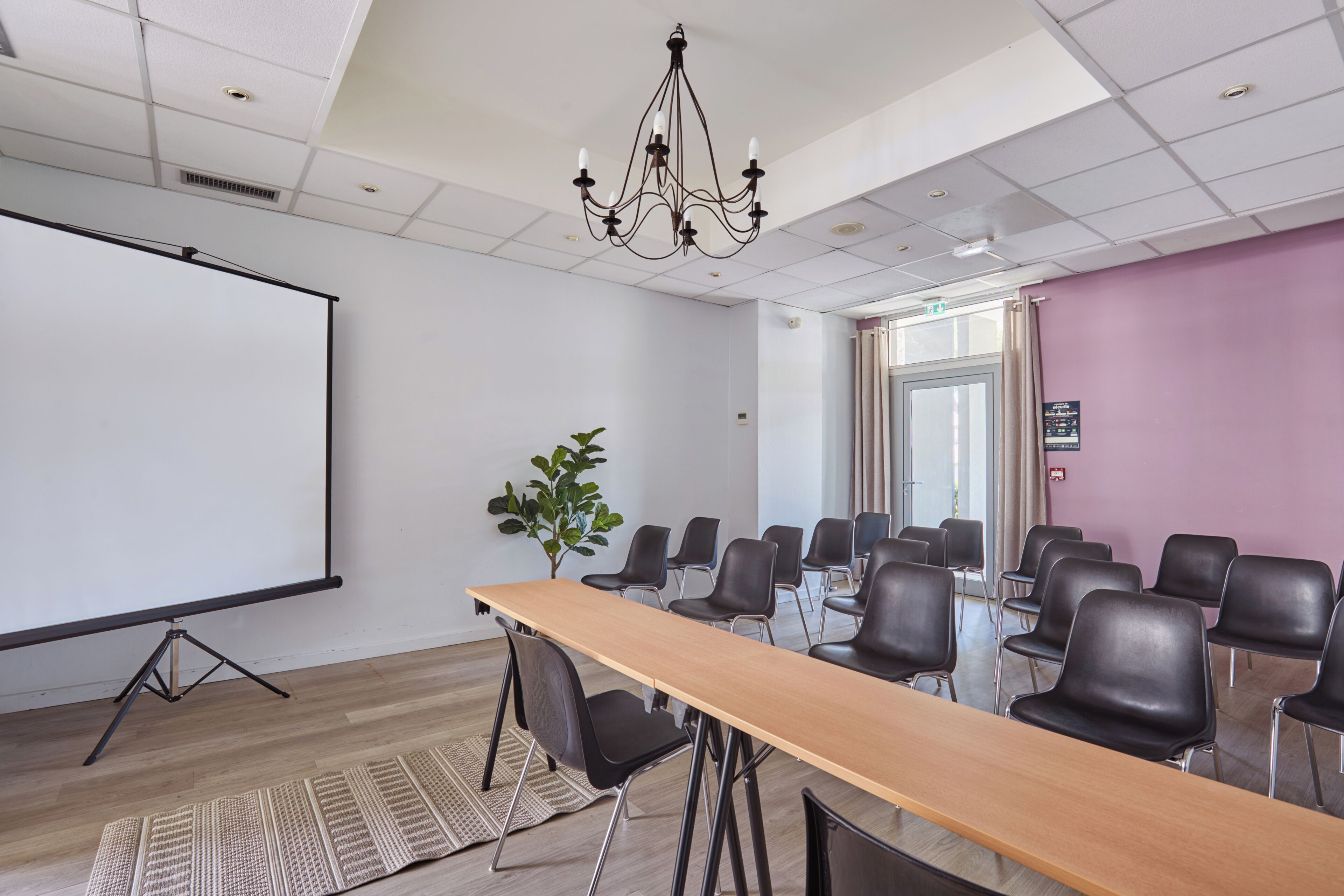 Ein Konferenzraum mit langem Tisch, Stühlen, einer Projektionsleinwand und einer Kandelaberleuchte.
