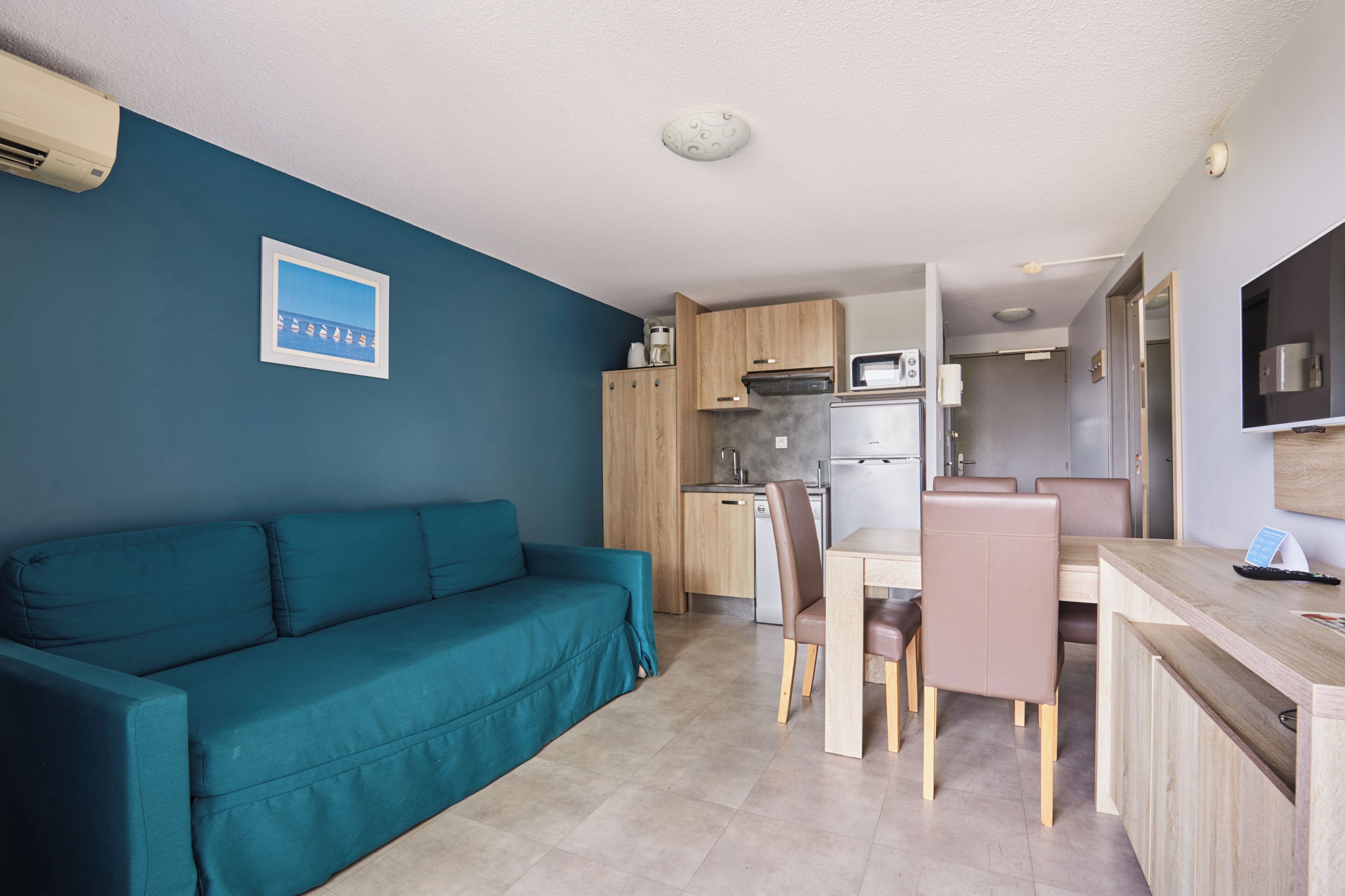 Un espace de vie compact comprenant un canapé de couleur turquoise, une table à manger avec des chaises, un coin cuisine et un petit espace cuisine.