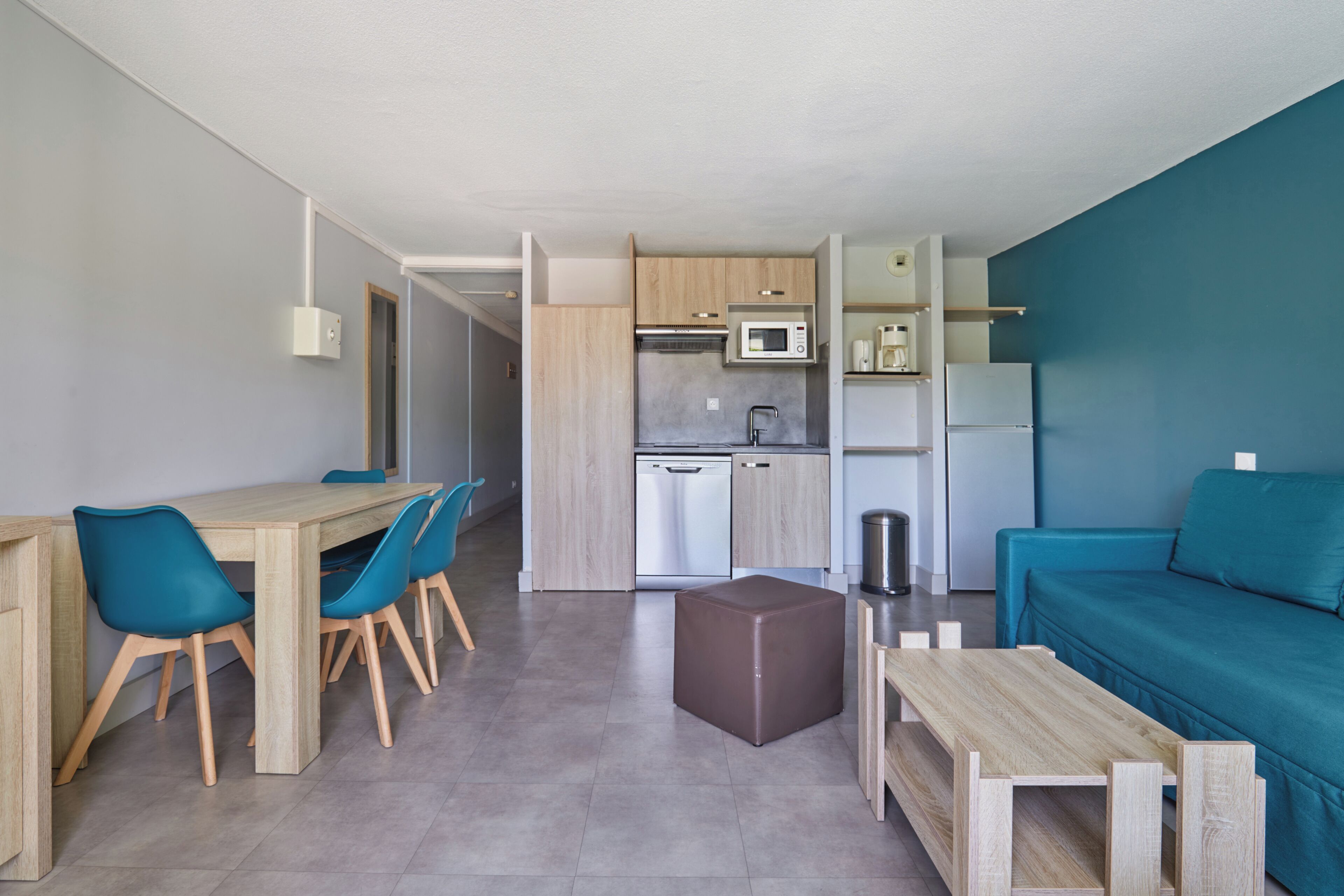 Una cucina moderna con microonde, forno ed elettrodomestico lavastoviglie. C'è un'area pranzo con tavolo e sedie in legno e un divano color petrolio.