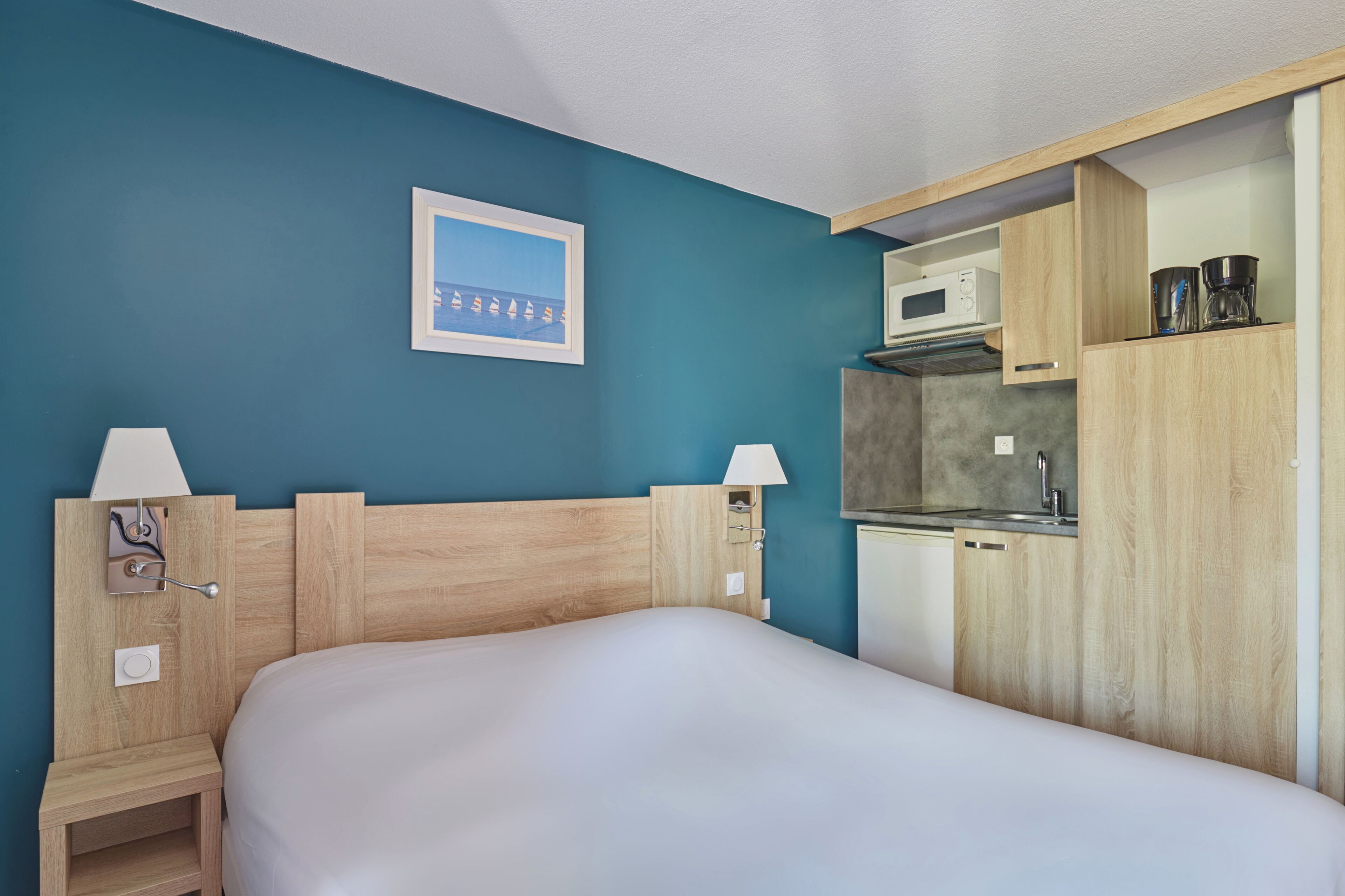 Une chambre comprenant un lit, une table de chevet, une lampe, un four à micro-ondes et un petit coin cuisine.