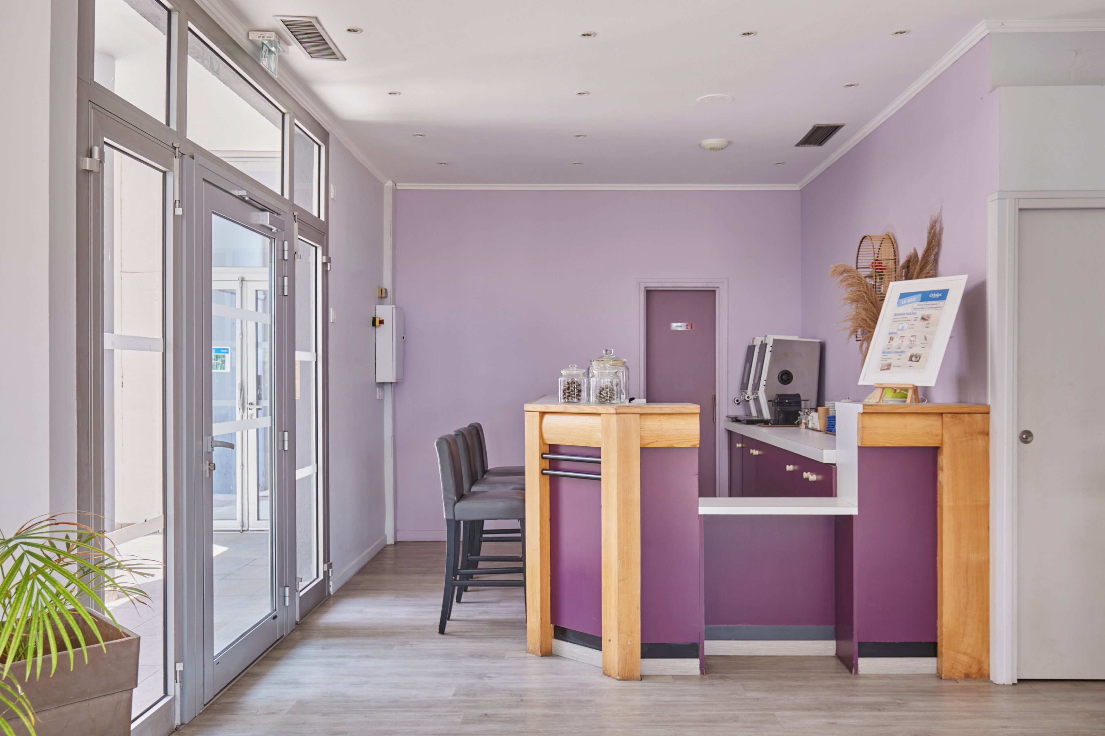 Un espace d’accueil comprenant un comptoir, des chaises, une porte et une grande fenêtre.