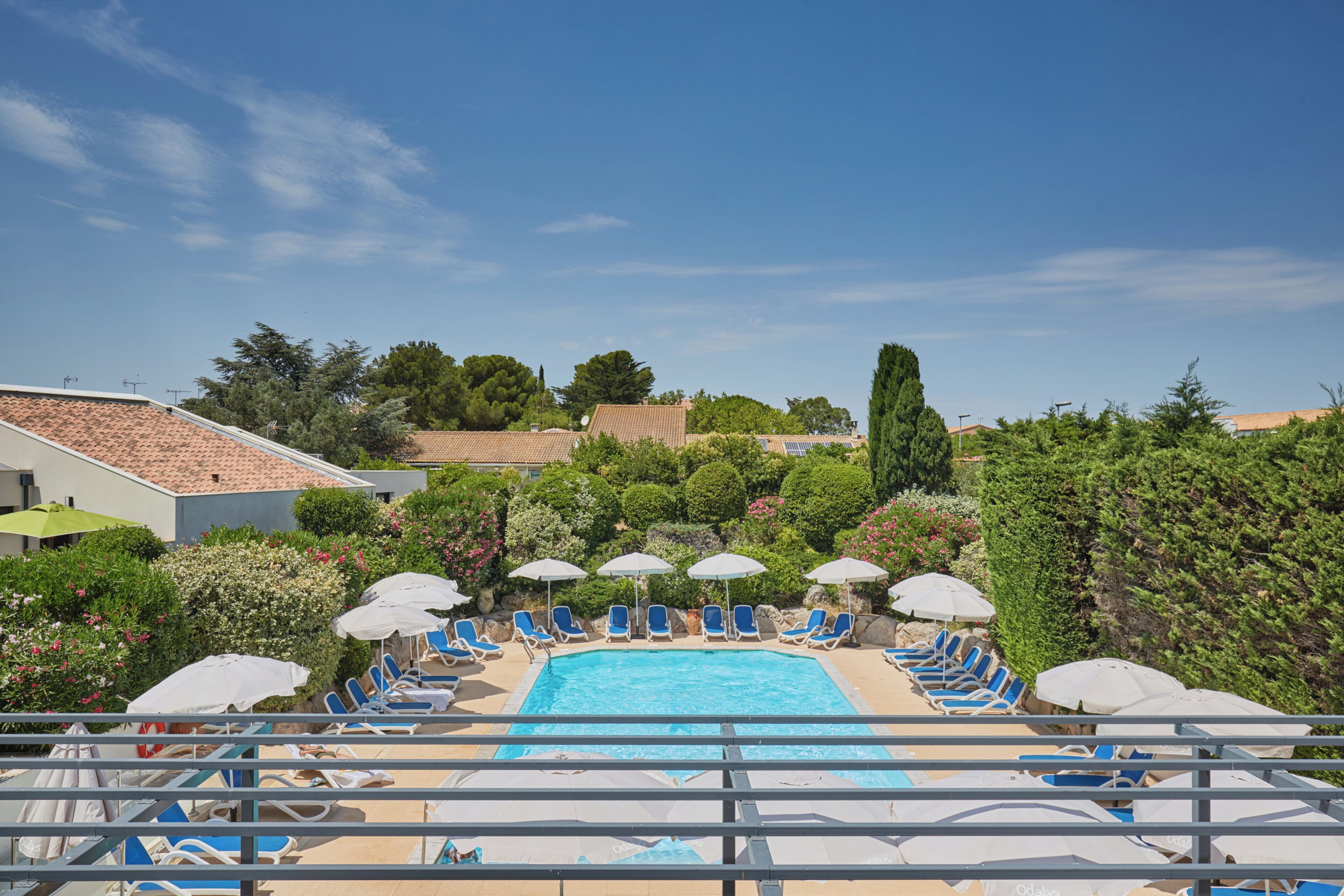 A swimming pool with lounge chairs and umbrellas, surrounded by greenery and buildings.