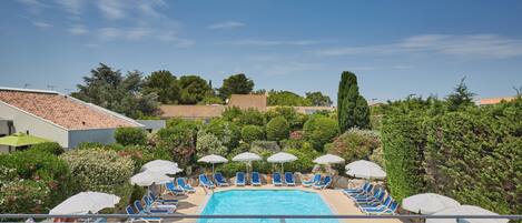 A swimming pool with lounge chairs and umbrellas, surrounded by greenery and buildings.