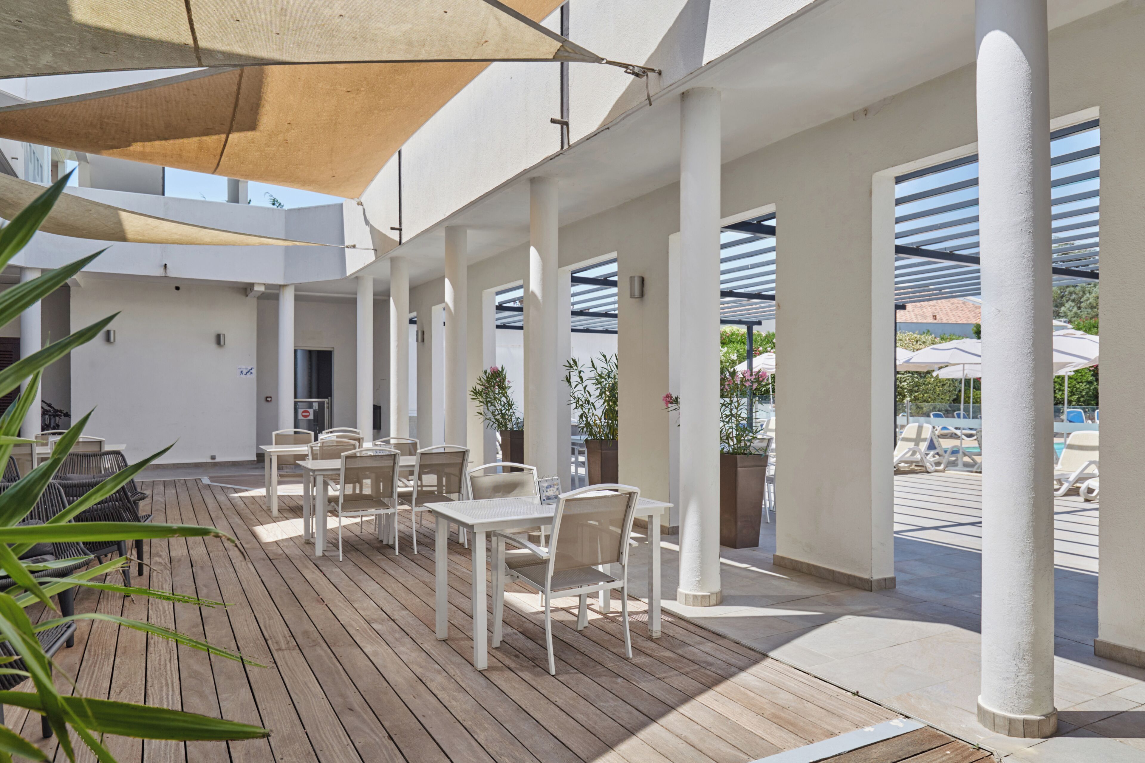 Een overdekt terras met tafels, stoelen, zuilen en potplanten.