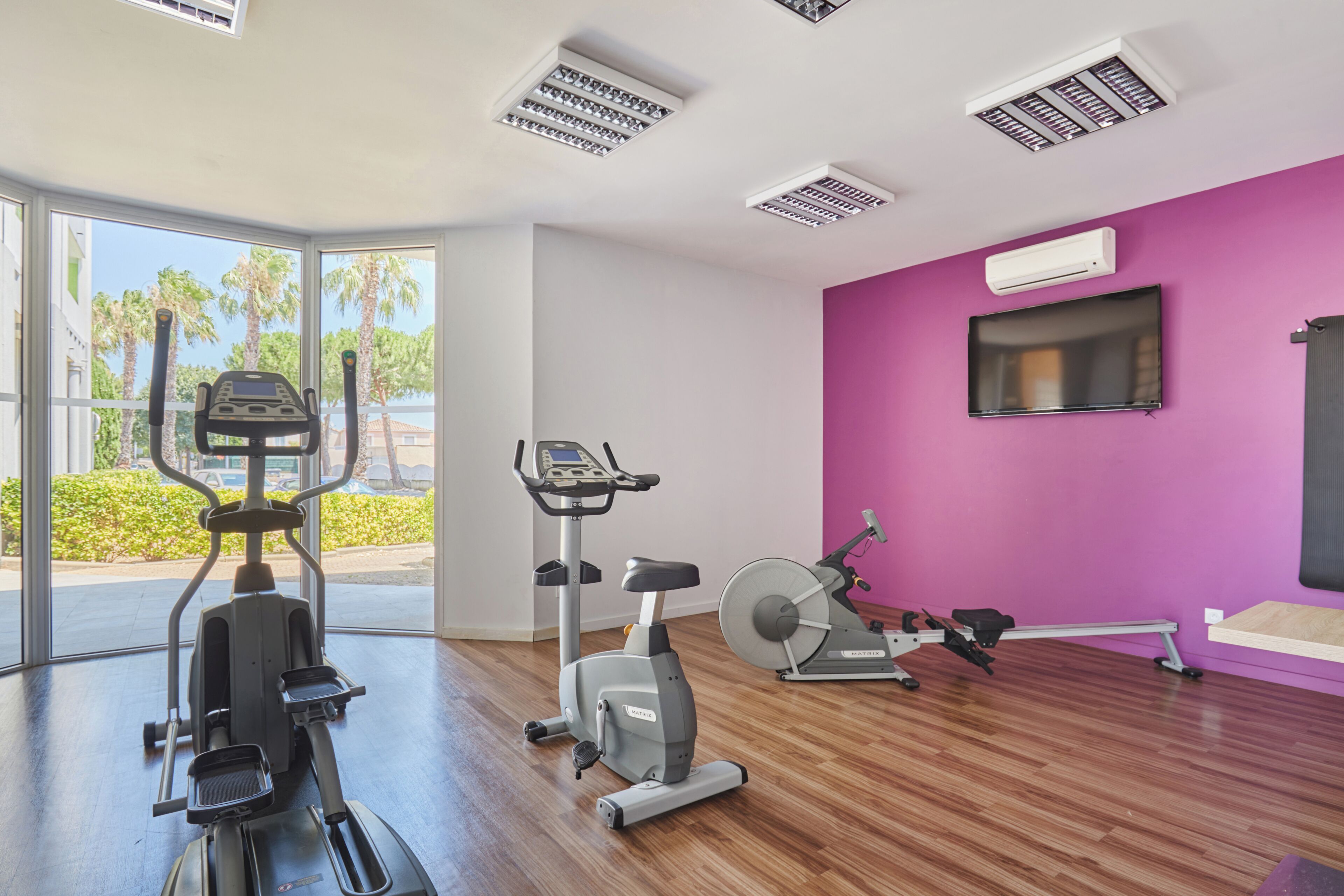 A gym with exercise equipment, a TV, and a purple wall.