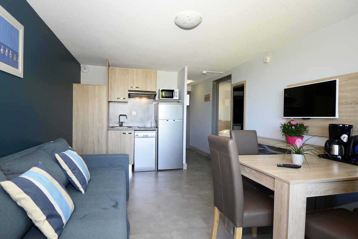 A compact living space with a kitchenette, a dining area, and a sofa with striped cushions.