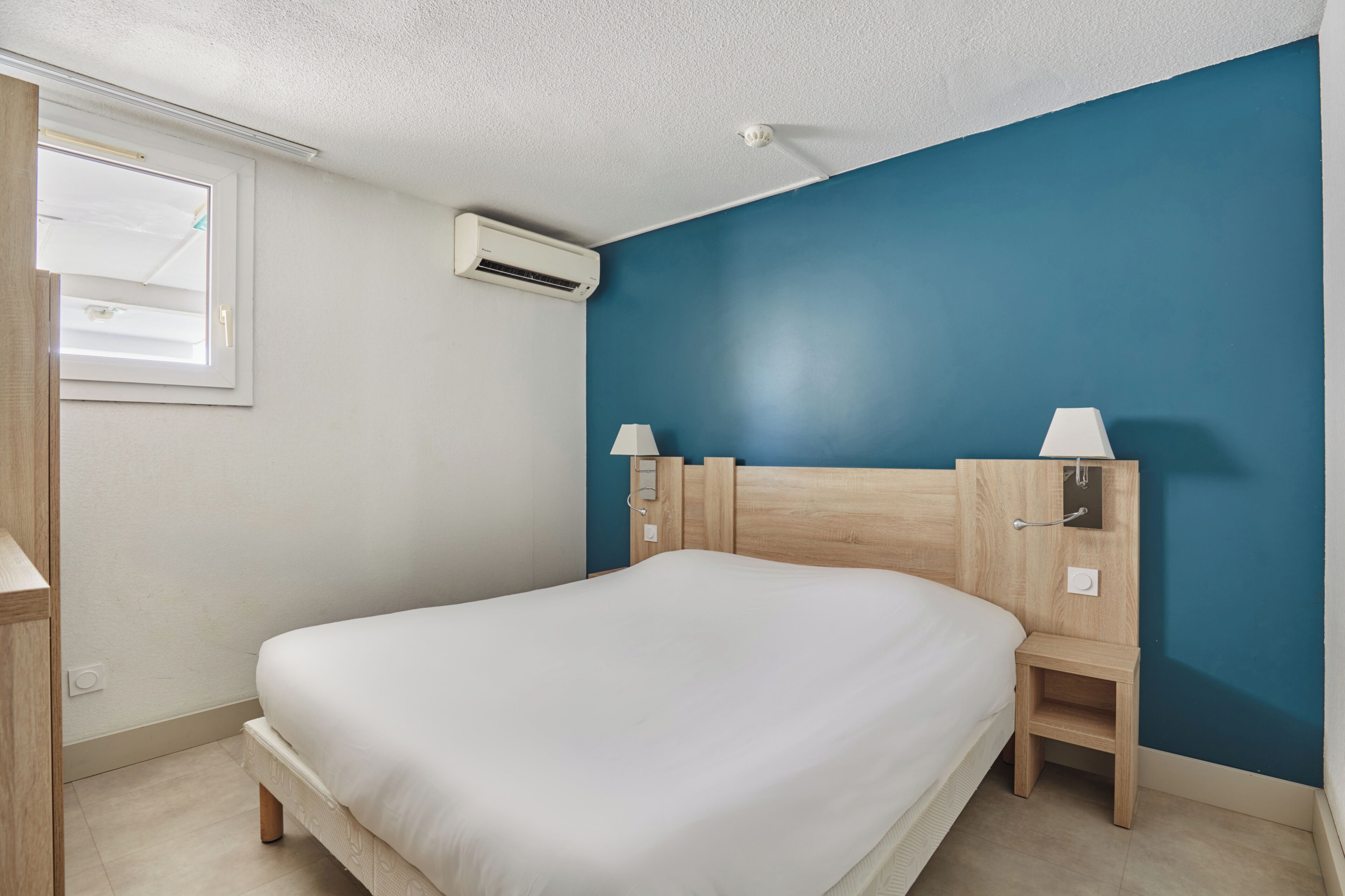 Ein Schlafzimmer mit einem Bett, einem Nachttisch, einer Wandklimaanlage und einem Fenster.