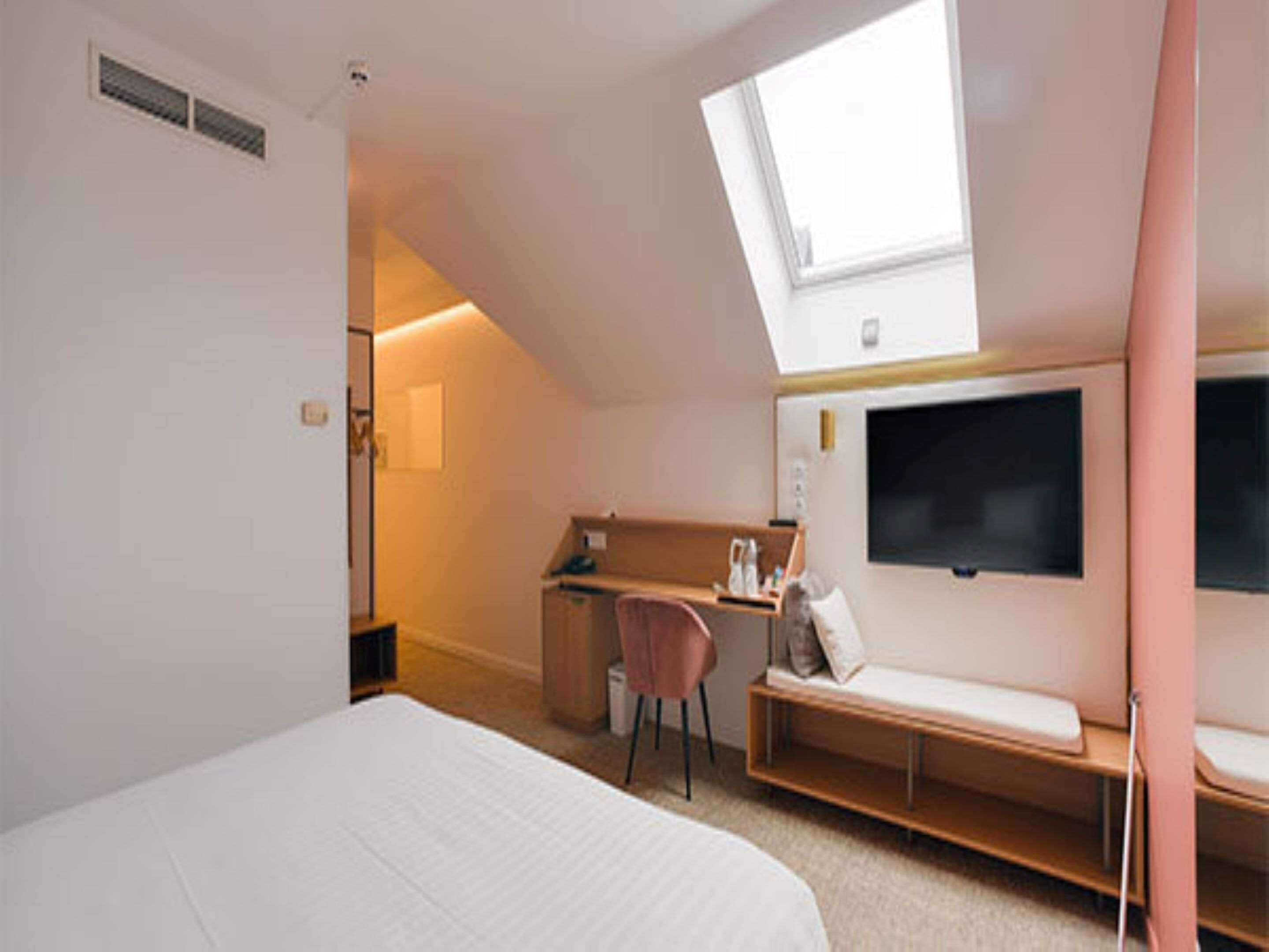 A bedroom with a skylight, a bed, a desk, a chair, and a TV.